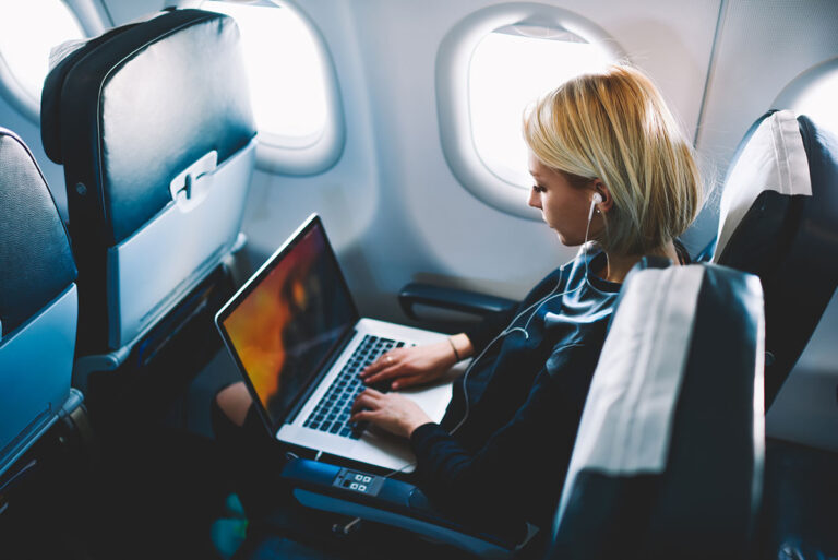 A lady in a plane working in a laptop and an earphone.