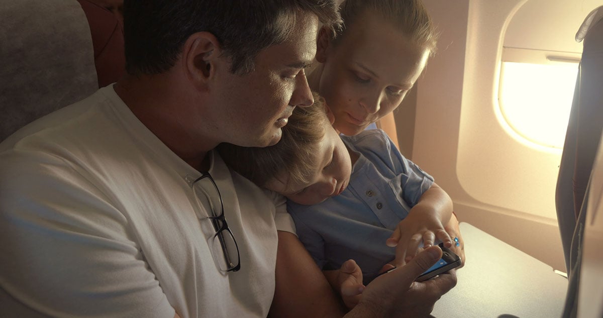 A small family on a plan playing on a phone.