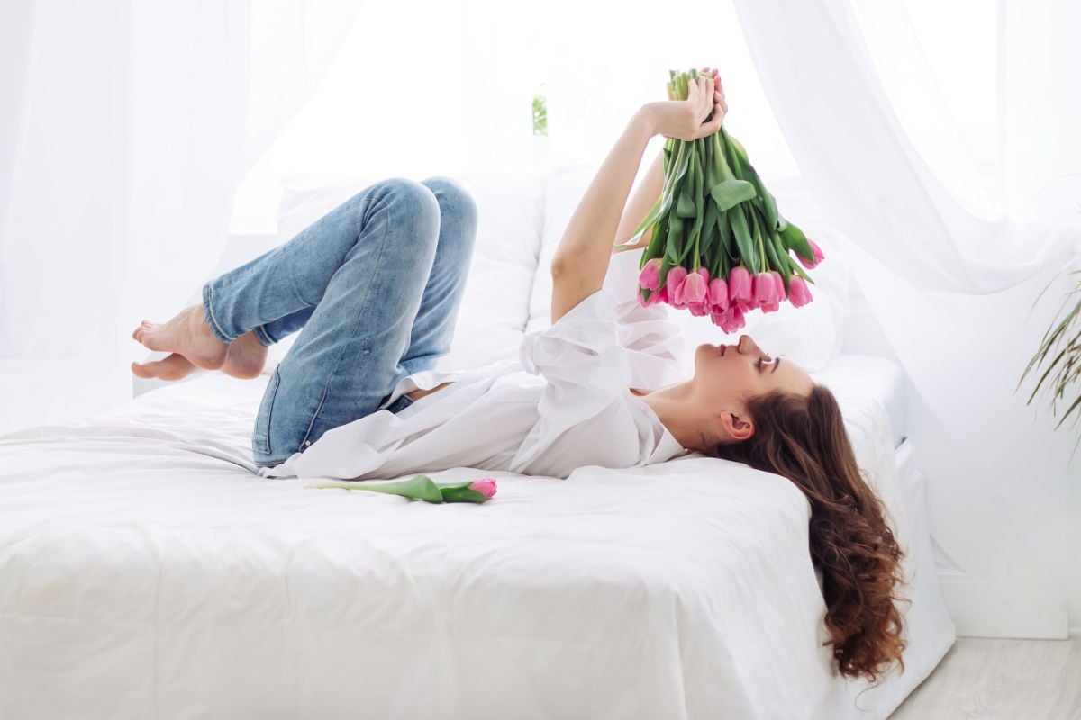 A woman lying on a hotel room smelling tulips.