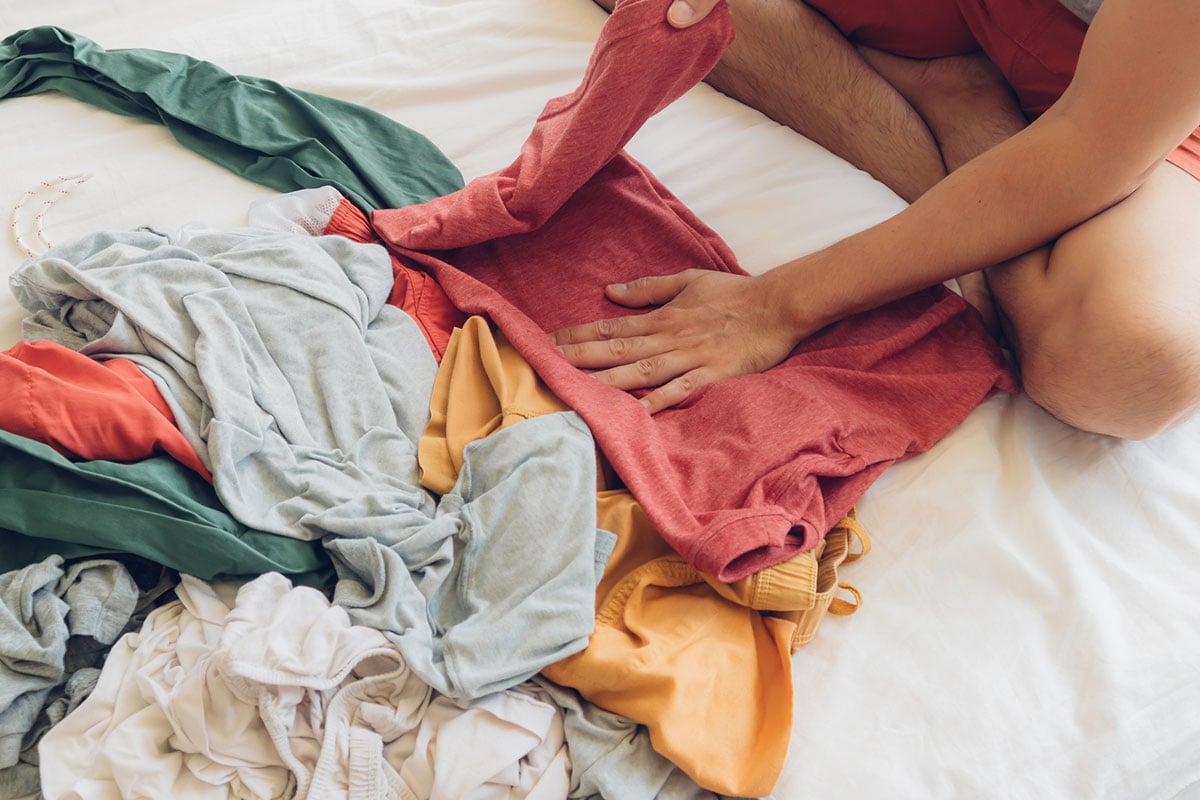 A man folding a clothes on top of a hotel bed.