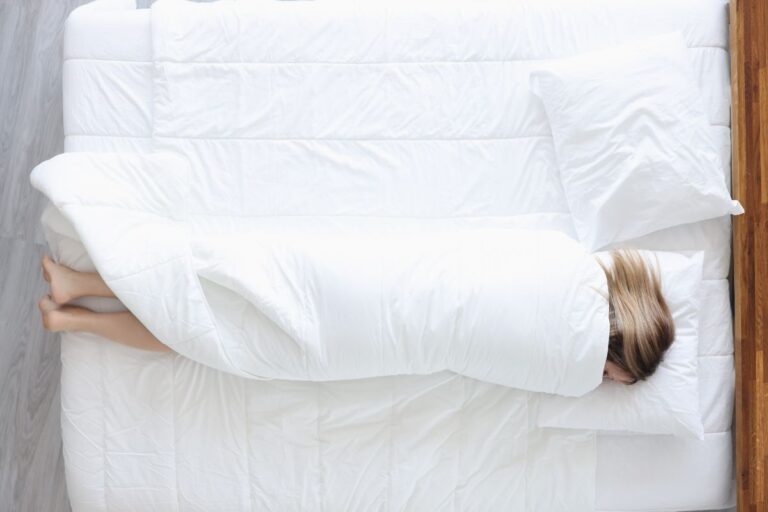 A woman on a hotel rolling in white sheets.