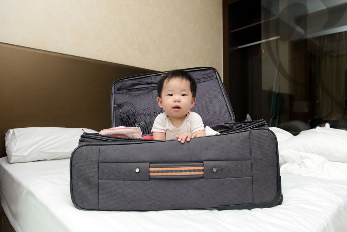 A baby in a large baggage on a hotel room.