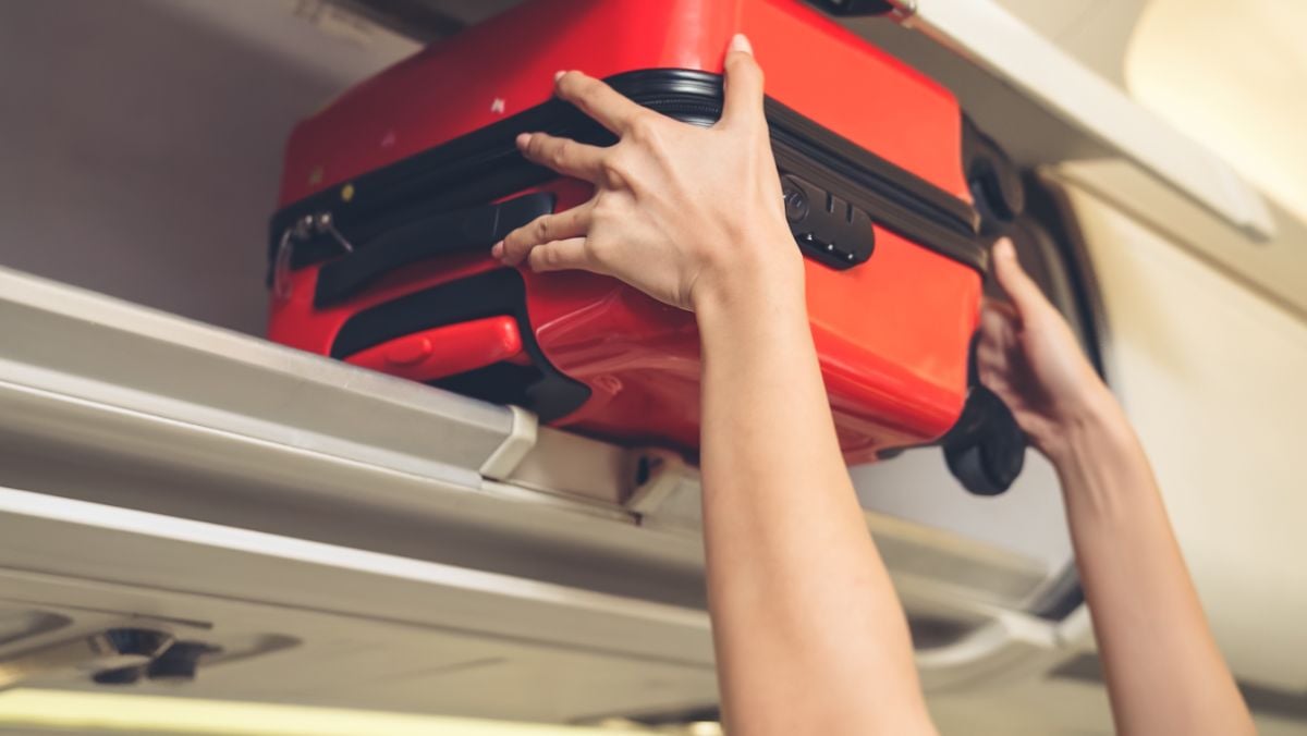 A person putting his luggage on the cabin.