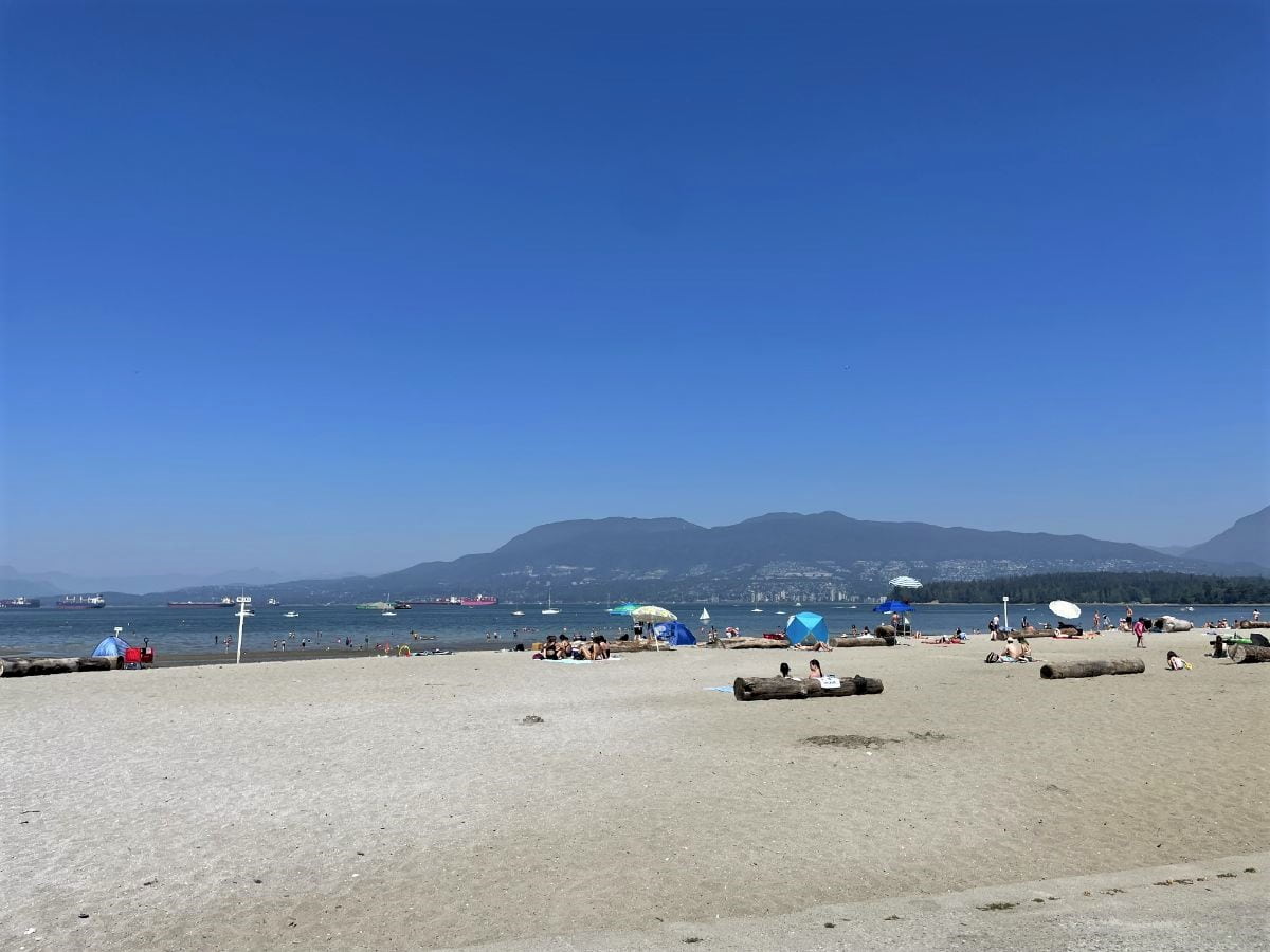 view of the ocean from kits beach in vancouver on a summer day with mountains in the background and boats on the water