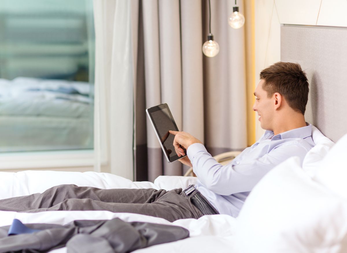 A person holding a tablet while lying on the bed.