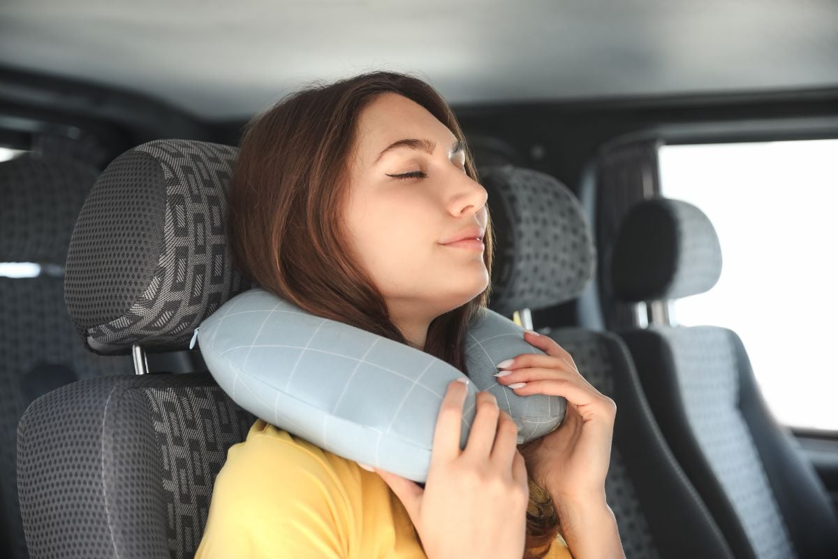 A woman resting on the car with her travel pillow.