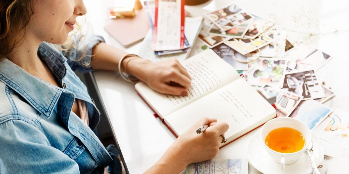 A woman writing on the journal and a cup of tea.