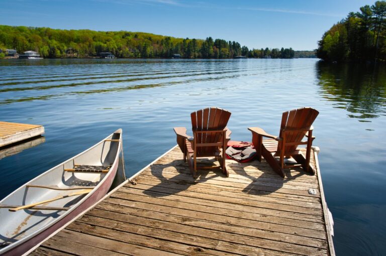 Two lake chairs sitting on a dock on a lake