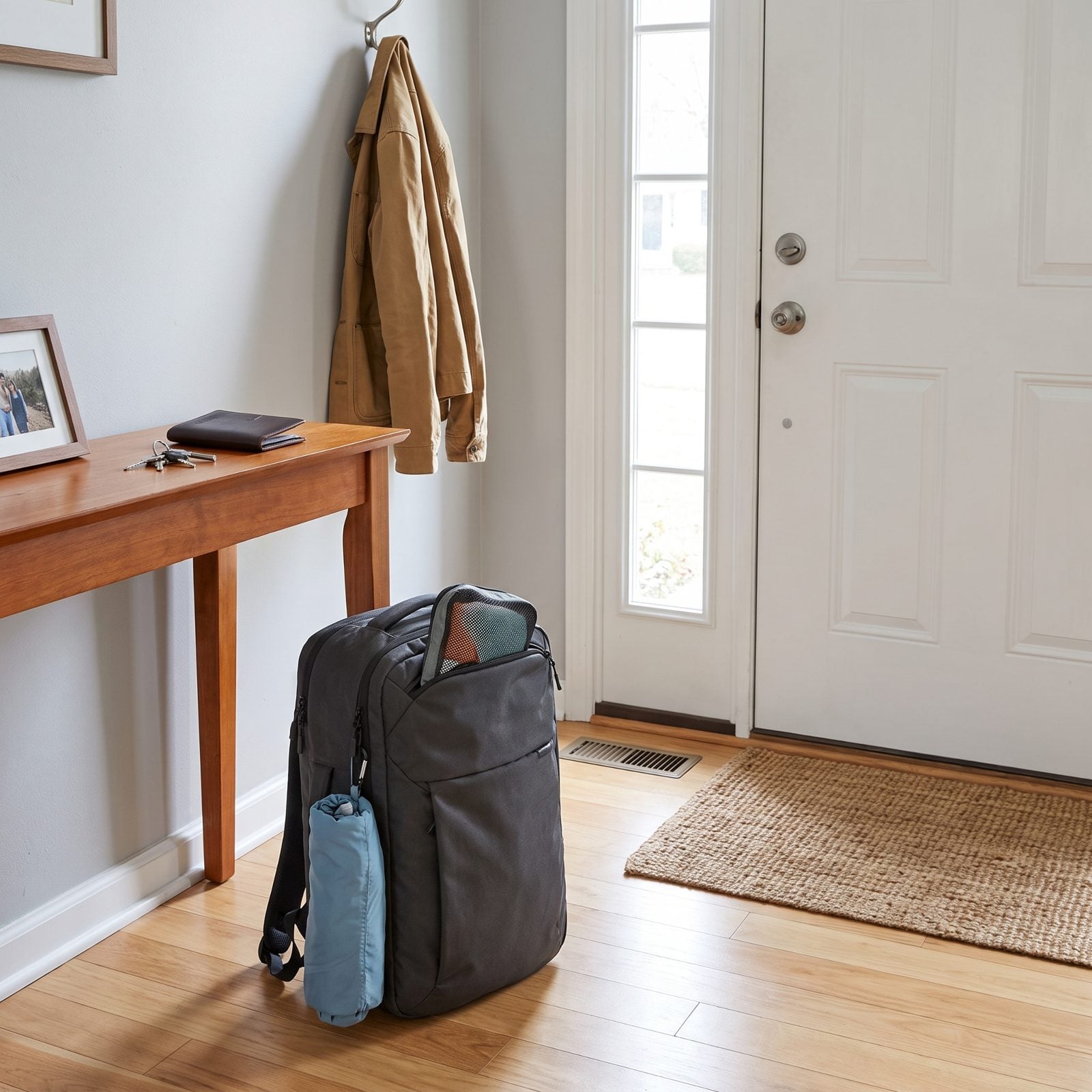 Entryway with a single carry-on backpack standing by the front door and keys on the console table.