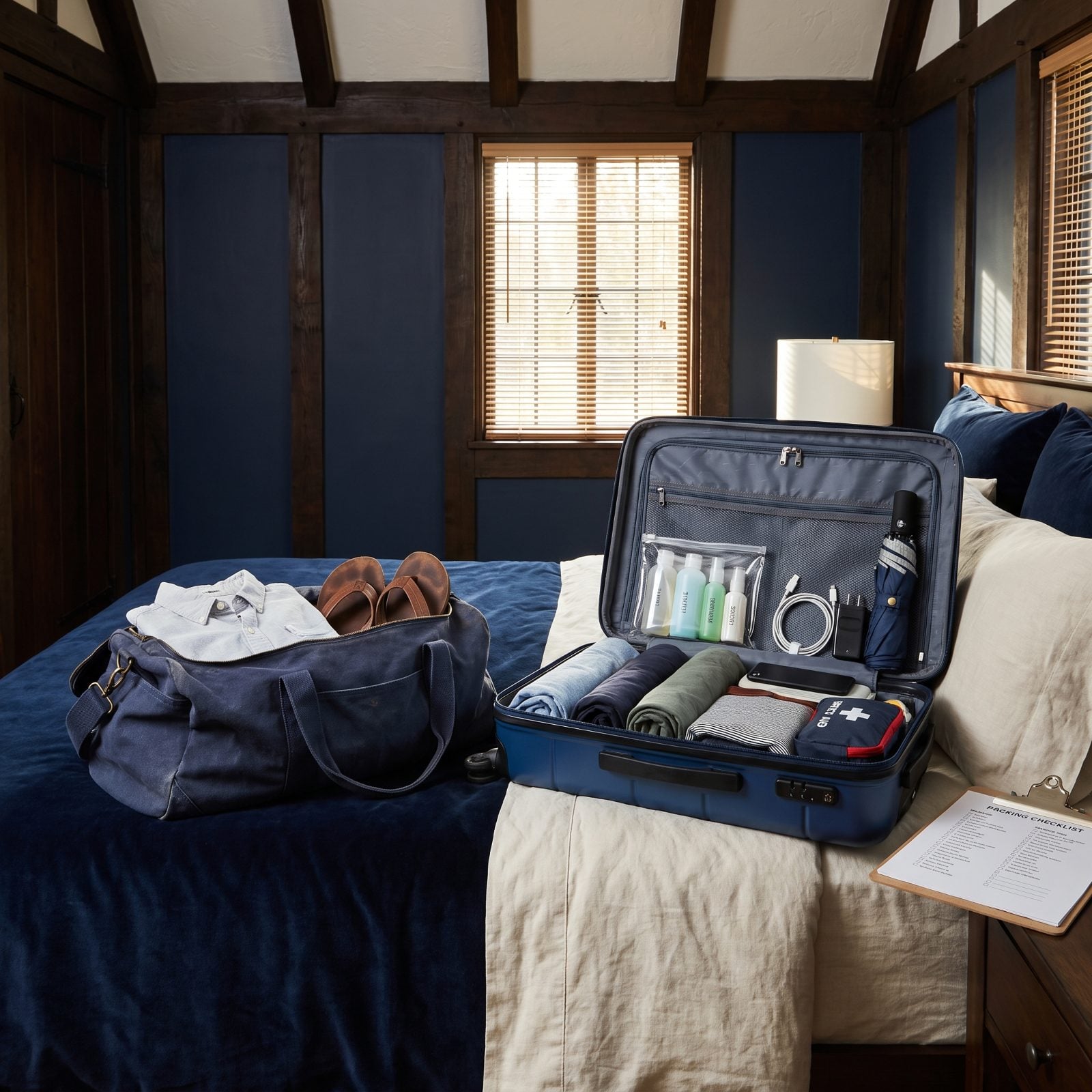 Bedroom with two open suitcases on a bed, a nearly empty soft duffel on the left and a fully packed hardside case with